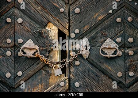 A locked lock hangs on a chain by old damaged gate with knockers Stock Photo
