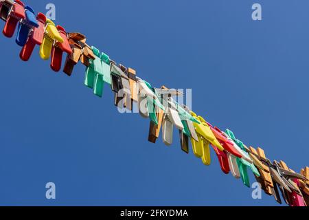 A colored clothes pegs hanging on a rope in nature. A group of clothespin in line against the blue sky. Stock Photo