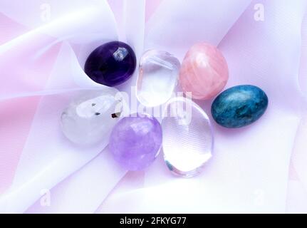 Gemstone minerals on a pink background. Round tumbling minerals of amethyst, rose quartz, rock crystal and apatite on white transparent fabric. Stock Photo