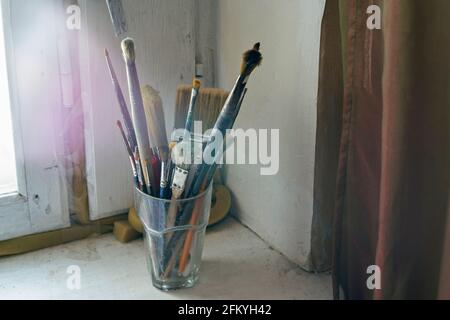 Painting brushes in the glass on the old windowsill. Selective focus on brushes. Blurred background Stock Photo