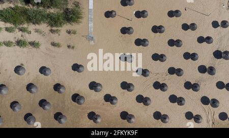 Bird's eye view of black thatch umbrellas stuck in the sand on a sunny beach Stock Photo