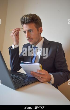 Vertical shot of a Spanish businessman holding pen and notebook while online meeting at home Stock Photo
