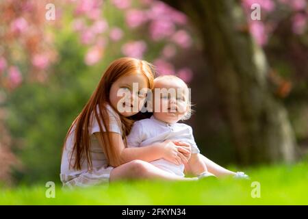 Young girl with her little baby brother outside on the grass Stock Photo