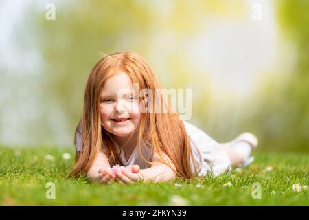 Six year old girl outside lying on the grass smiling Stock Photo