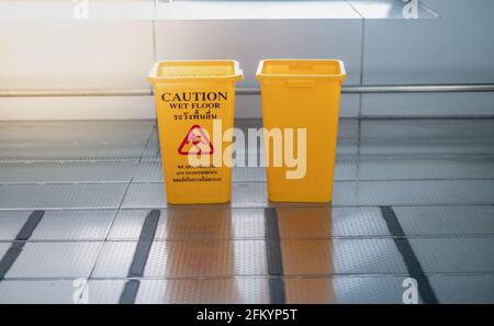 The yellow garbage bin and caution wet floor sign for the people . The Public trash on the side of the way to parking car in the airport Stock Photo