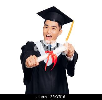 young man in  black graduation gown and cap holding a diploma isolated on white background Stock Photo