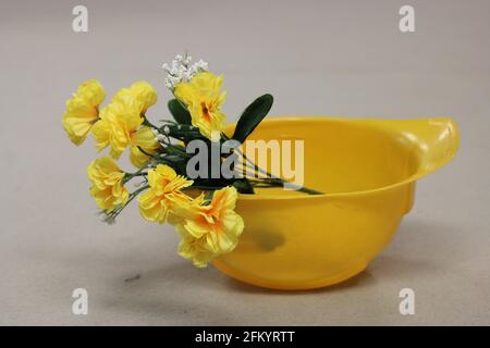 Bunch of yellow flowers , in yellow hard hat, on tan background Stock Photo