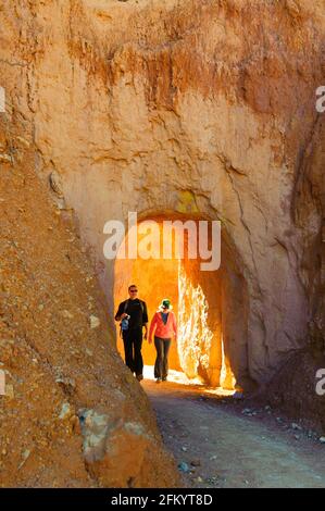 Backlit couple hiking in a tunnel going through a hoodoo, Bryce Canyon National Park, Utah, USA. Stock Photo