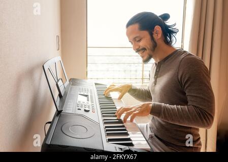 Young latin man learning to play piano at home during quarantine Stock Photo