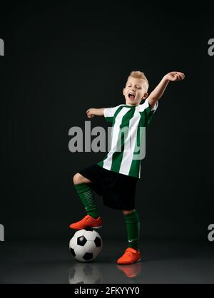 Soccer school student, boy in red white uniform stands with ball under his foot and holds arms outstretched Stock Photo
