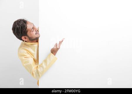 Indian man holding white board, promoting offers on festival season while wearing traditional cloths, standing over white background. Stock Photo