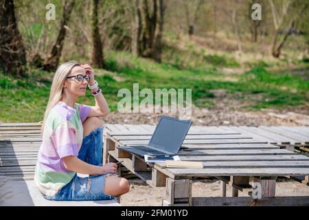 Freelance blonde woman with glasses works outdoors. Stock Photo