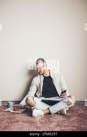 concentrated freelancer using tablet and phone write working at home on the floor having a coffee Stock Photo