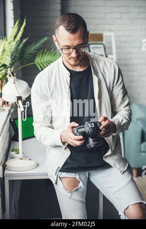 Balding photographer is using a photo camera at home wearing glasses while looking at the screen Stock Photo