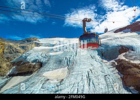 Titlis, Engelberg, Switzerland - Aug 27, 2020: cable car with Swiss flag moving to Titlis icy peak of snowy Uri alps. Located in cantons of Obwalden Stock Photo