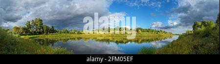 Stormy dramatic sky over the calm lake and green hills during sunset.Beautiful panoramic landscape. Stock Photo