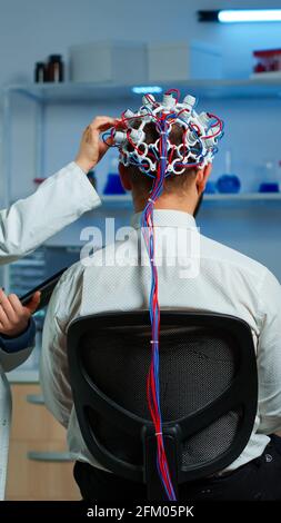 Man patient wearing performant eeg headset scanning brain electrical activity in neurological research laboratory while medical researcher controlling it, examining nervous system, nurse taking notes Stock Photo
