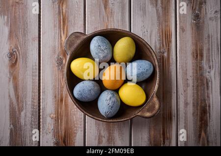 Homemade Easter multi-colored painted eggs on ceramic platter against a background of textured boards. Top view, copy space Stock Photo