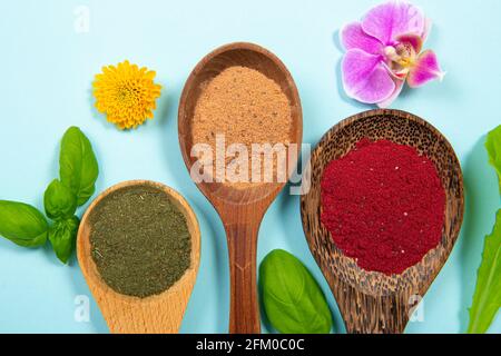 Flat lay view of various superfood powders on spoon decorated with flower blossoms and leaves on blue studio background. Vibrant colorful picture red, Stock Photo