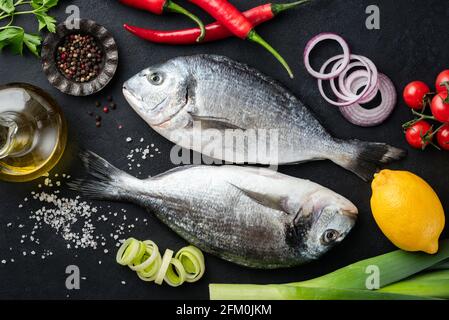 Two uncooked dorado fishes on black background with spices and vegetables for cooking, top view Stock Photo