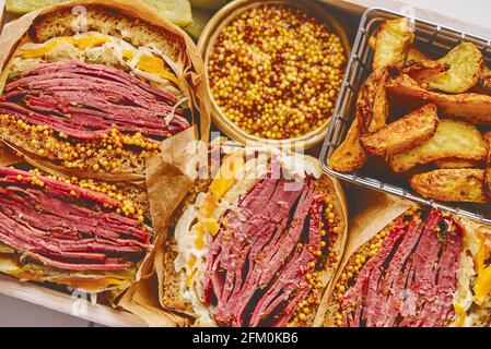 Enormous sandwiches with pastrami beef in wooden box. Served with baked potatoes, pickles Stock Photo