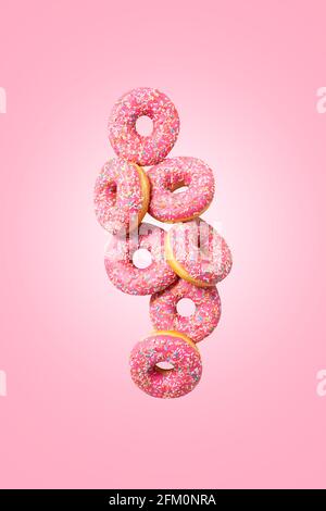 Amazing donuts on soft pink background. Top view of yummy fresh homemade doughnuts. Decorated with confetti in shape of little hearts. Levitation.  Stock Photo