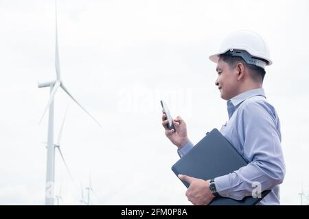 Success engineer windmills using smartphone and holding laptop with the wind turbine in background Stock Photo