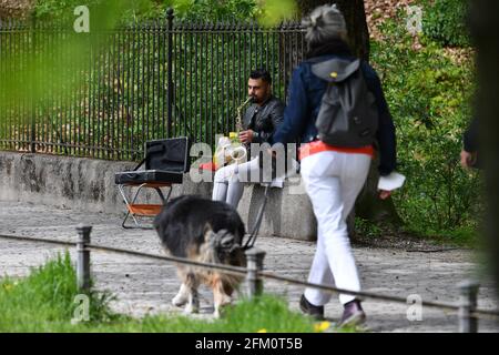Munich, Germany. 05th May, 2021.  Street musician in times of the coronavirus pandemic: A man plays the saxophone in Munich-a passer-by walks past him with her dog on a leash. Street musician, musician, | usage worldwide Credit: dpa/Alamy Live News Credit: dpa picture alliance/Alamy Live News Stock Photo