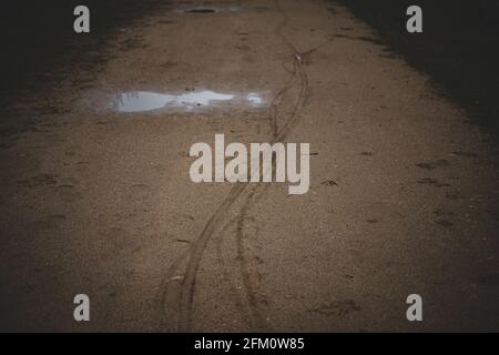 tracks in the sand - tires from bicycles and human shoes. puddle on gravel trail Stock Photo