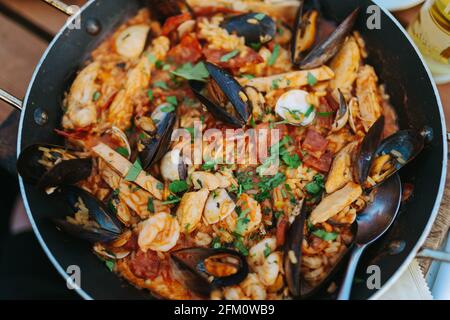 Classic dish of Spain, seafood paella in traditional pan on rustic wooden background top view. Spanish paella with shrimps, clamps, mussels, green Stock Photo