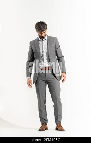 Handsome man in smart suit stood looking downwards on a white background Stock Photo