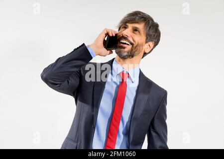Smiling businessman in jacket using mobile phone and looking upwards on white background. Stock Photo