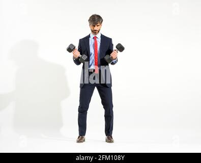 Smart businessman in suit lifting two dumbbell weights, white studio background. Stock Photo