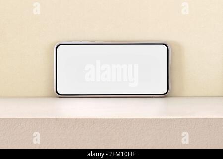 Contemporary mobile phone with empty screen for data placed on shelf against light yellow wall Stock Photo