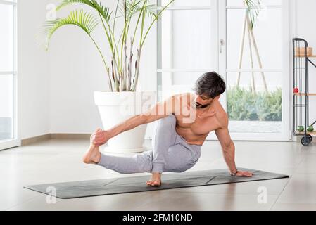 Athletic sporty man doing a yoga balance pose stretching to grasp his toes to increase mobility and strengthen his muscles in a high key gym with copy Stock Photo