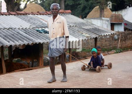 Bhakta tribal old man pulling small kids in a wooden toy cart at Hattaguda village, Andhra Pradesh, India Stock Photo