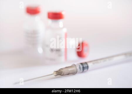 Thin syringe lies for single vaccination vials with red cap on a white background. Corona - Covid-19. Focus on the gray hub of the needle Stock Photo