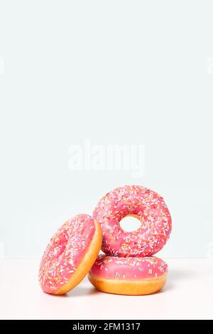 Cute fresh pink donuts in stack. Vertical format. Copy space on top. Light blue background. Donut day celebration.  Stock Photo