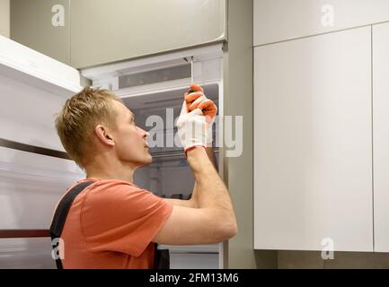 The worker is fixing the built-in refrigerator in the kitchen furniture. Stock Photo