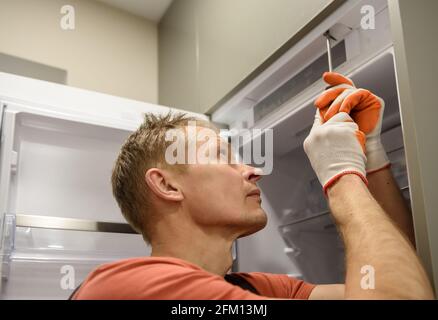 The worker is fixing the built-in refrigerator in the kitchen furniture. Stock Photo