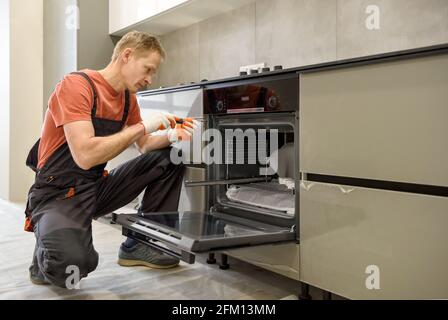 The worker is installing an electric oven in the kitchen furniture. Stock Photo