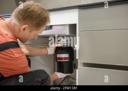 The worker is installing a household waste shredder for the kitchen sink. Stock Photo