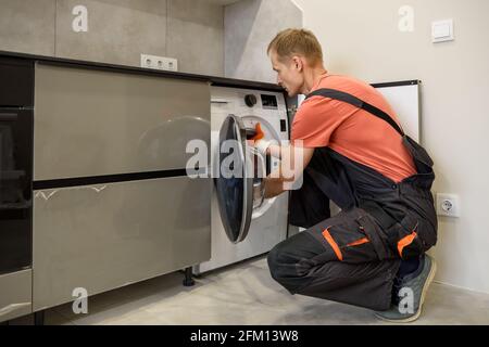 The worker is installing a washing machine in the kitchen furniture. Stock Photo
