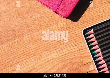 Overhead image of a pink notebook and a tray of colored pencils on a wooden surface Stock Photo