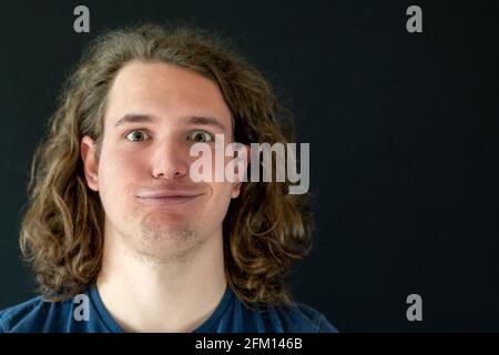 Portrait of a Middle Eastern man with long curly hair and a big smirk on black background Stock Photo
