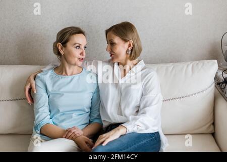 Two adult women are sitting on the couch talking to each other. Stock Photo