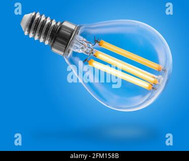 Energy efficient led filament Light Bulb Glowing isolated on blue background. Stock Photo