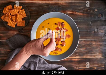 Woman's hand drips green oil from a pipette on traditional pumpkin puree cream soup with carrots, onions, ginger, garlic, coconut milk. Healthy, vegetarian food. Top view, selective focus Stock Photo