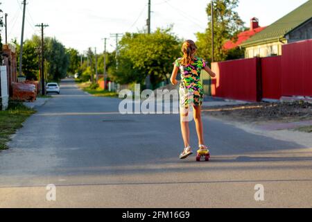 Defocus happy young girl playing on skateboard in the street. View from back. Caucasian kid riding penny board, practicing skateboard. Sport lifestyle Stock Photo