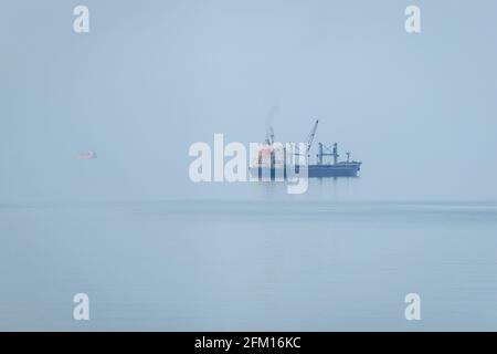 Cargo ship anchored in the sea on a foggy morning.  The sea merges with the horizon.  Batumi, Georgia. Photo with soft focus. Stock Photo